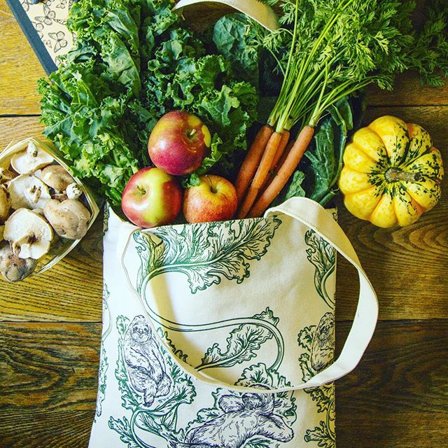 Photo of tote bag full of vegetables with lazy sloth illustrations on it on wood backdrop