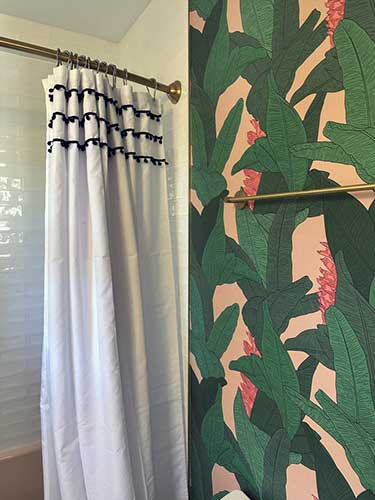 Photo of bathroom with large banana leaf wallpaper on walls, shower curtain and pink bathtub